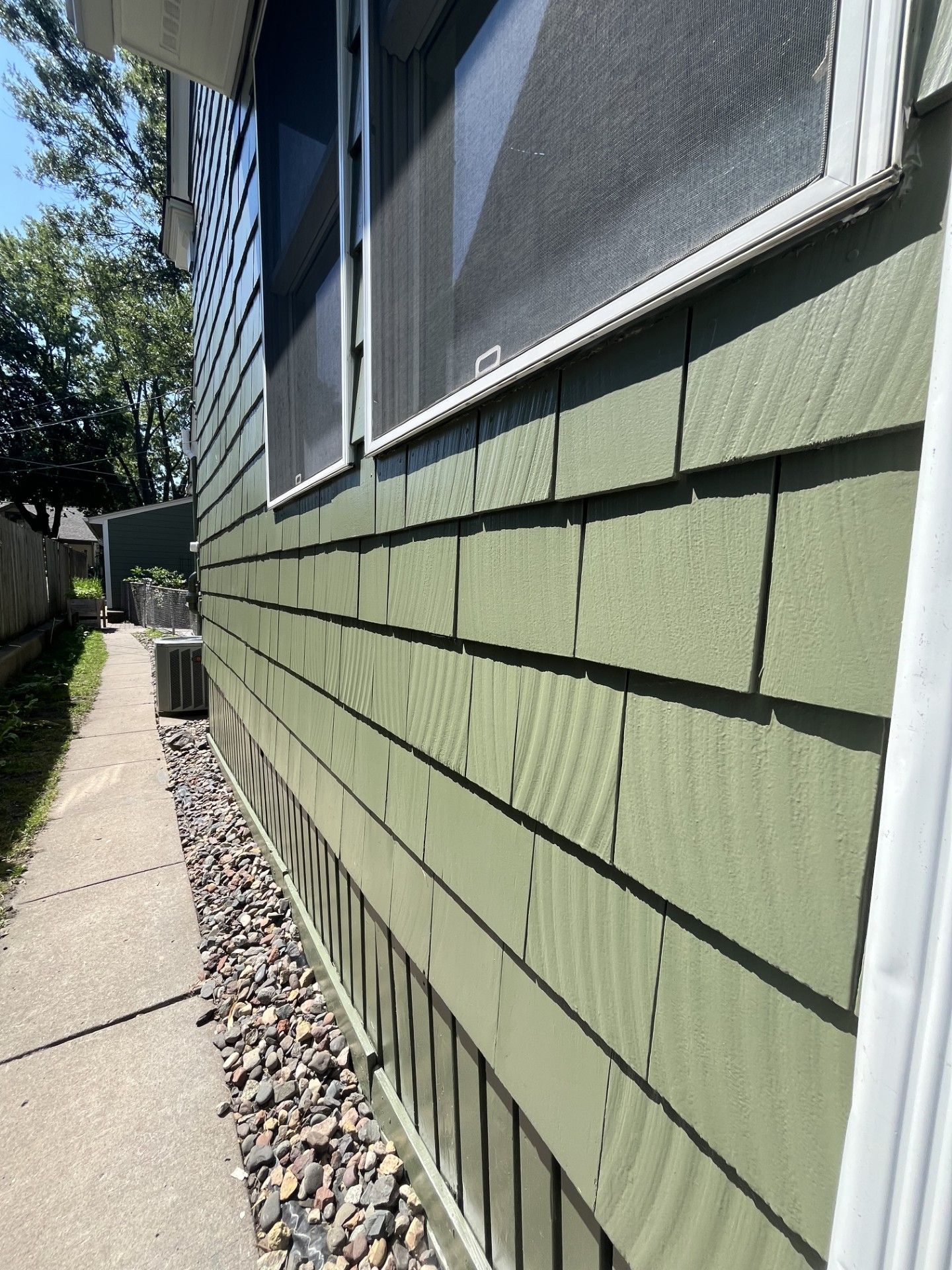 Green-sided house with a sidewalk, rocks, and a window.