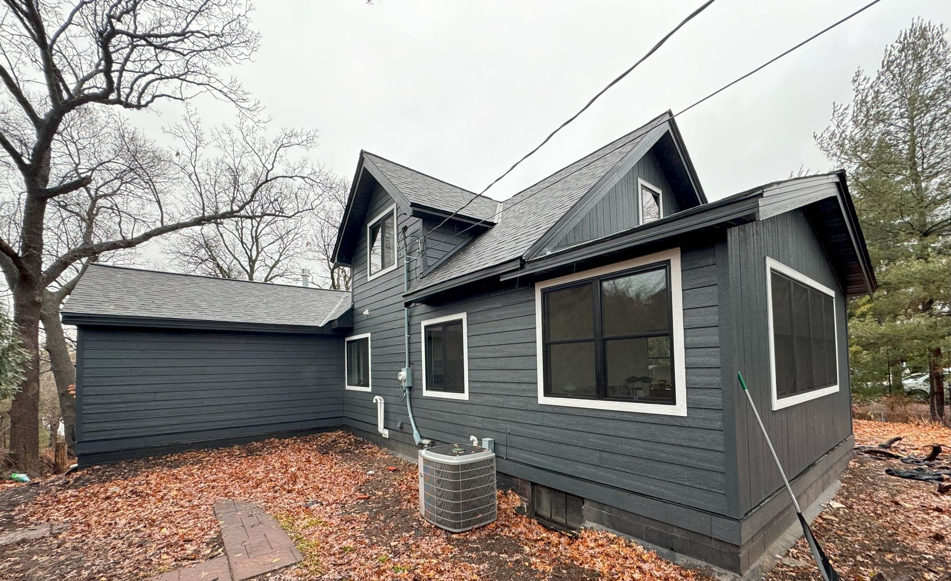 A black house with a lot of windows is surrounded by trees and leaves.