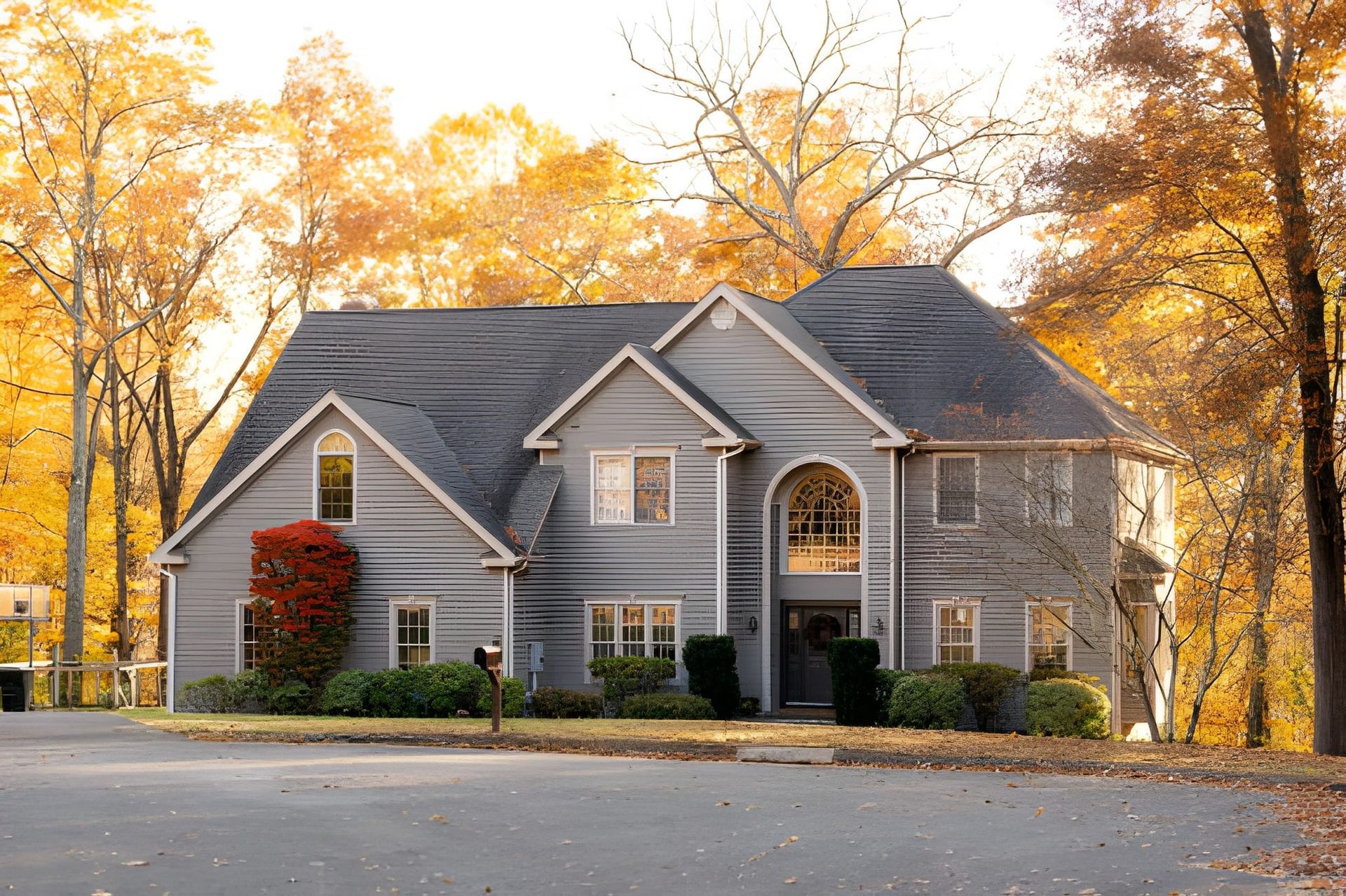 Two-story gray house with black roof, surrounded by golden autumn trees. Front door visible.