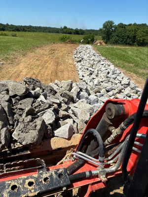 Red tractor spreading gravel on a rural road beside green fields under a clear sky