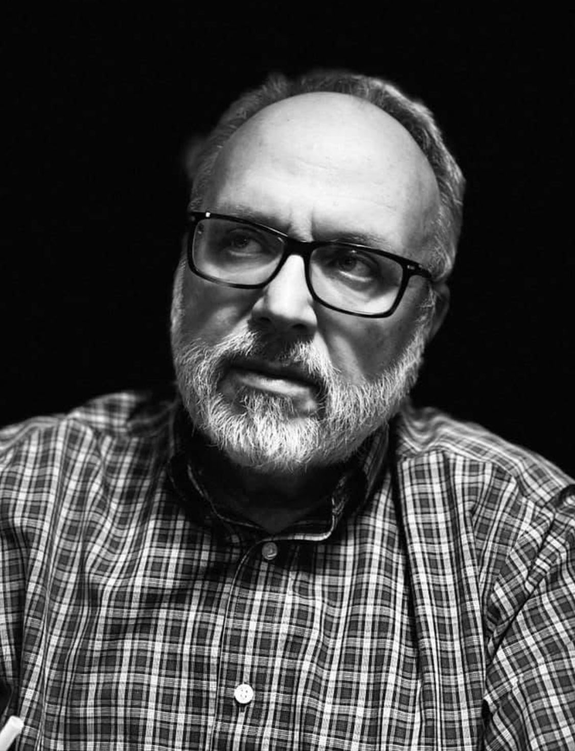 Man wearing glasses and a plaid shirt, looking off-center with a thoughtful expression.