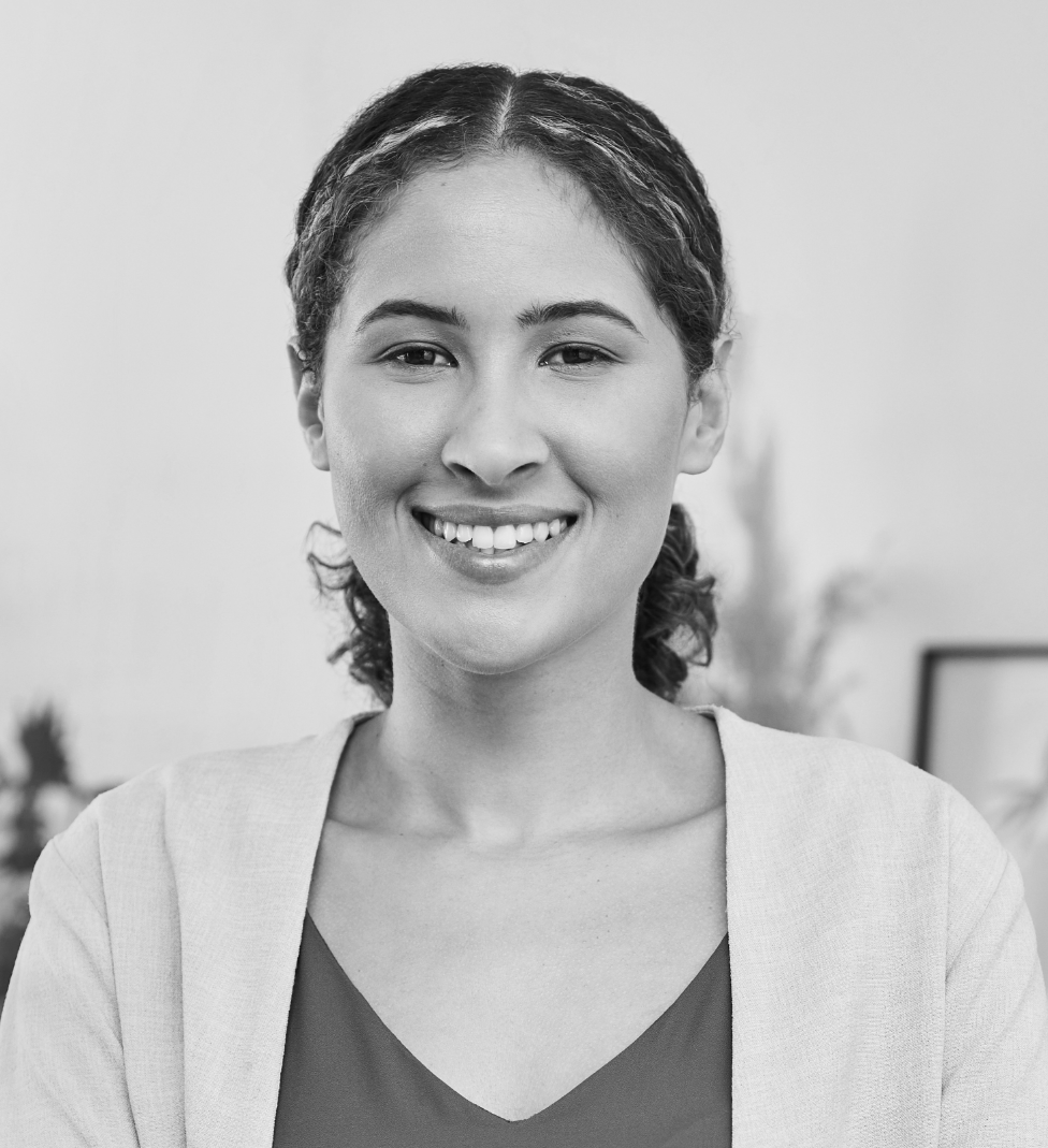 Smiling woman in a light cardigan and dark top, standing indoors against a blurred background