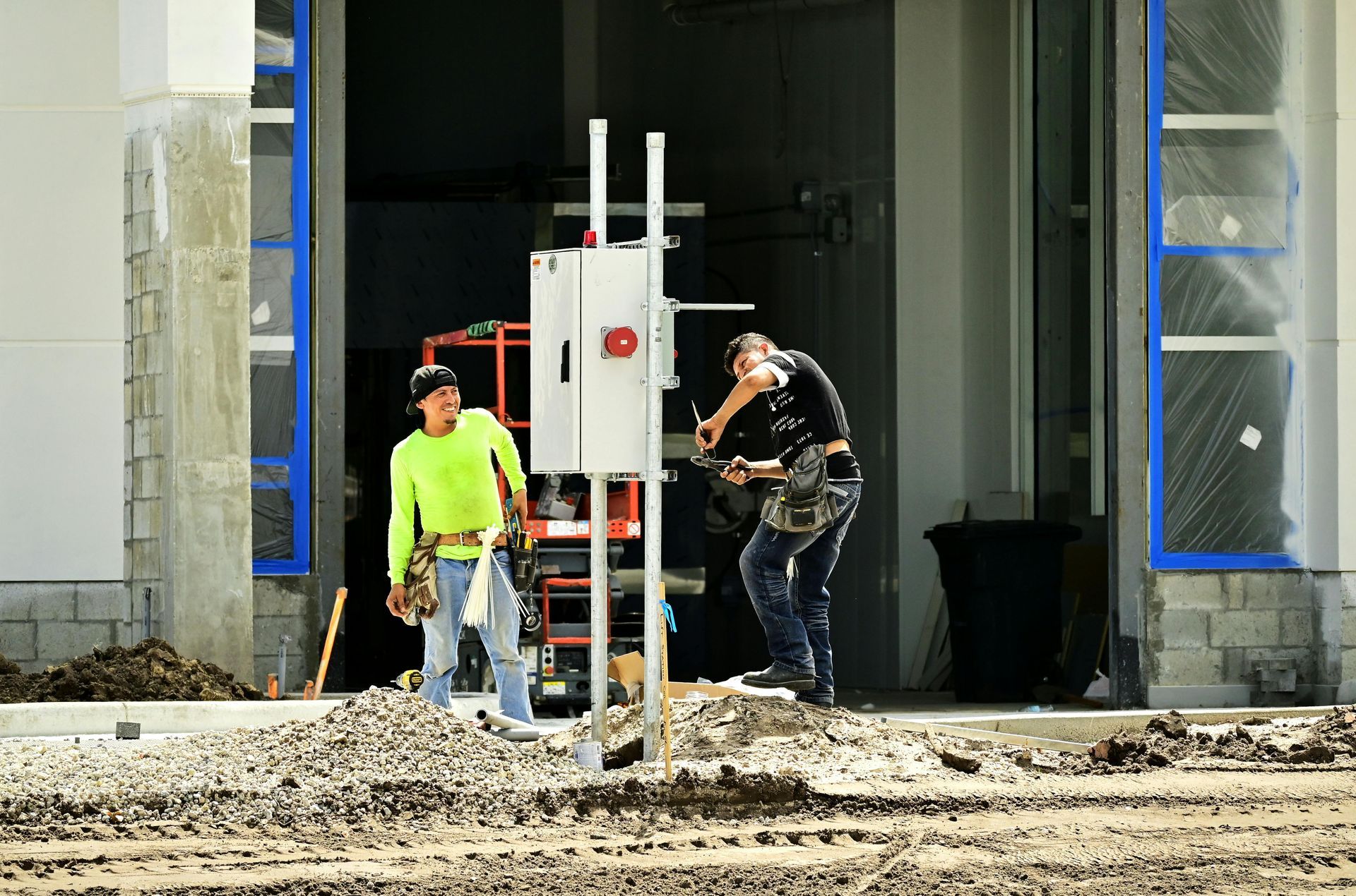 Two workers in safety gear working at a construction site entrance with equipment and debris