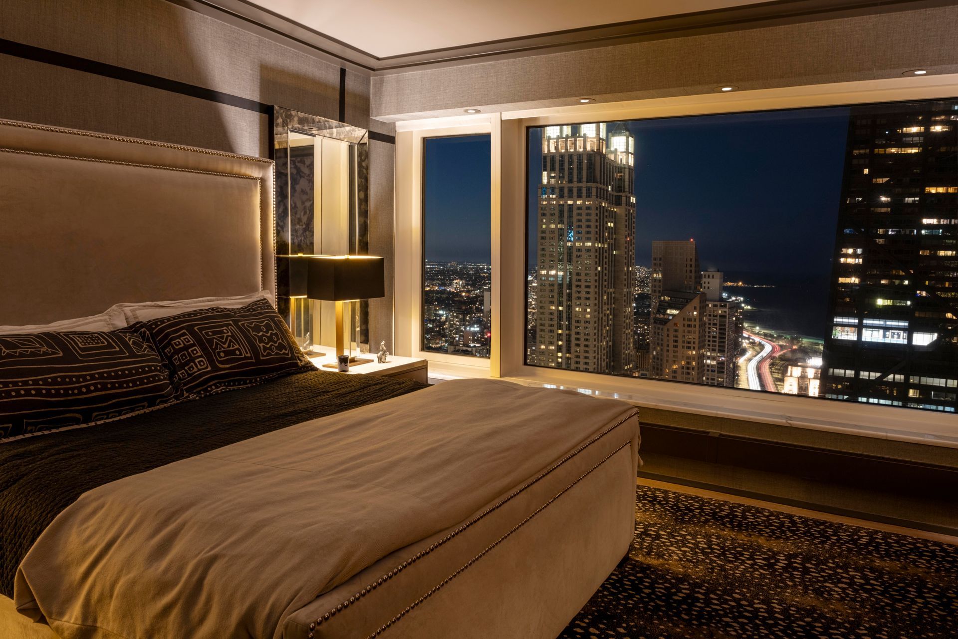 A bedroom with a large bed and a view of the city at night