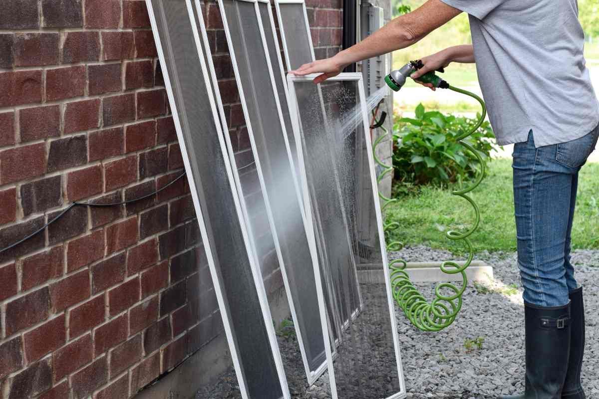A homeowner wearing rain boots hosing off their window screens outside after cleaning them near Tustin, CA