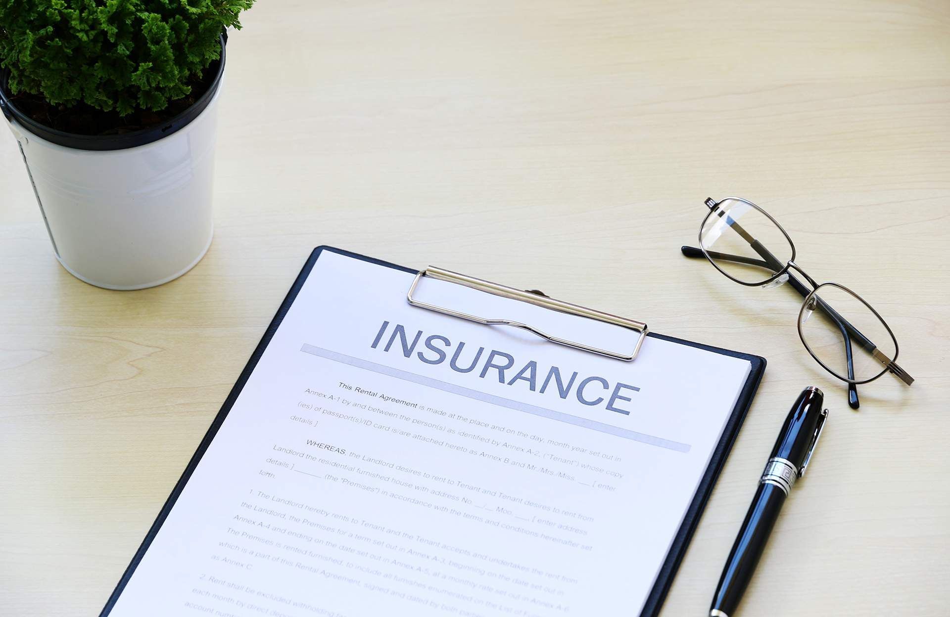 Insurance form on a desk with glasses, a pen, and a small potted plant.