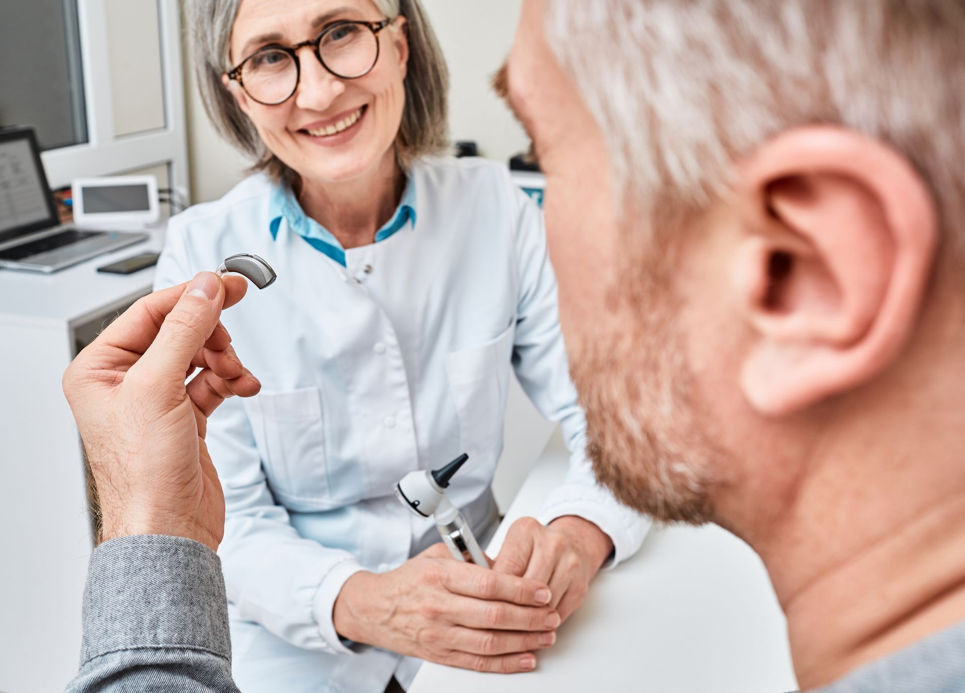 A doctor is putting a hearing aid in an older man 's ear