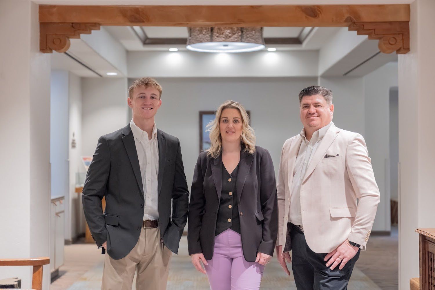 Three professionals standing in a bright hallway, smiling at the camera.