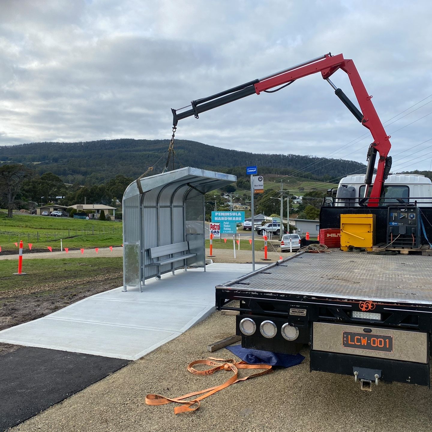 Crane lowering a metal shelter onto a concrete pad at an outdoor construction site