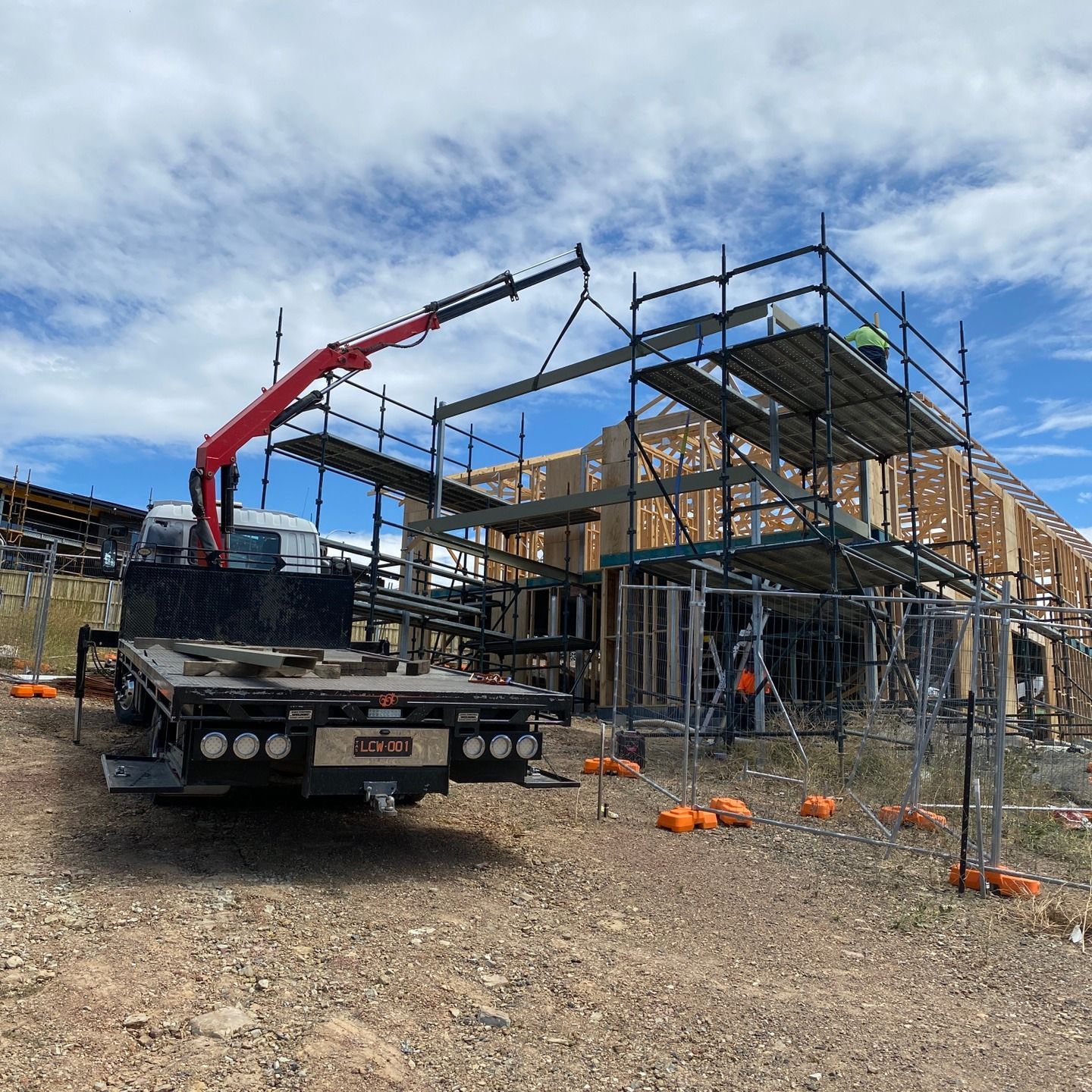 Construction site with a crane truck lifting scaffolding beside a partially framed building