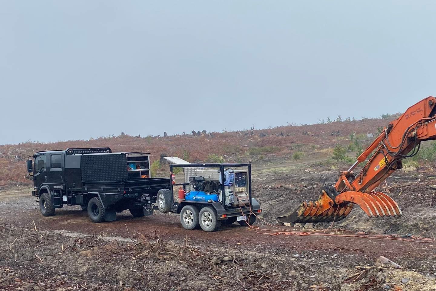Excavator loading debris into a dump truck and trailer on a barren hillside