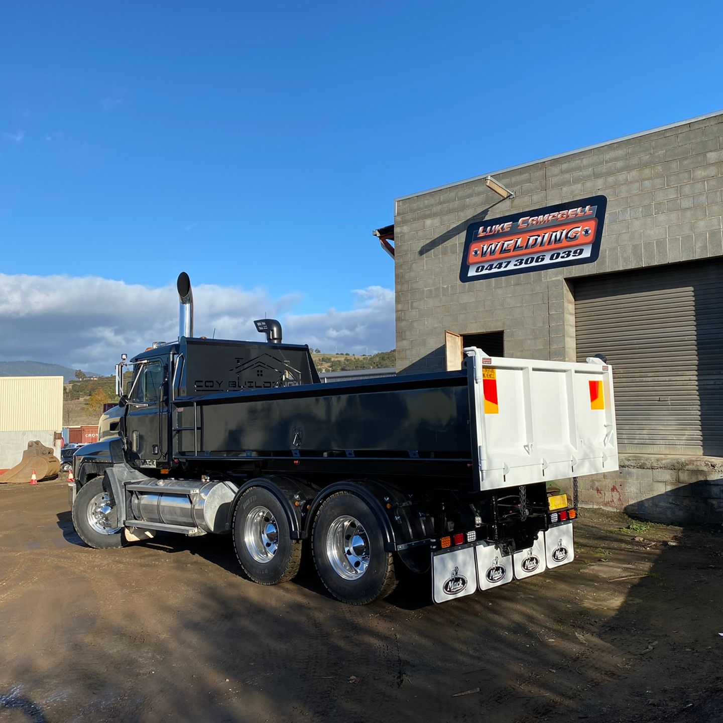 Black dump truck parked outside a garage on a sunny day