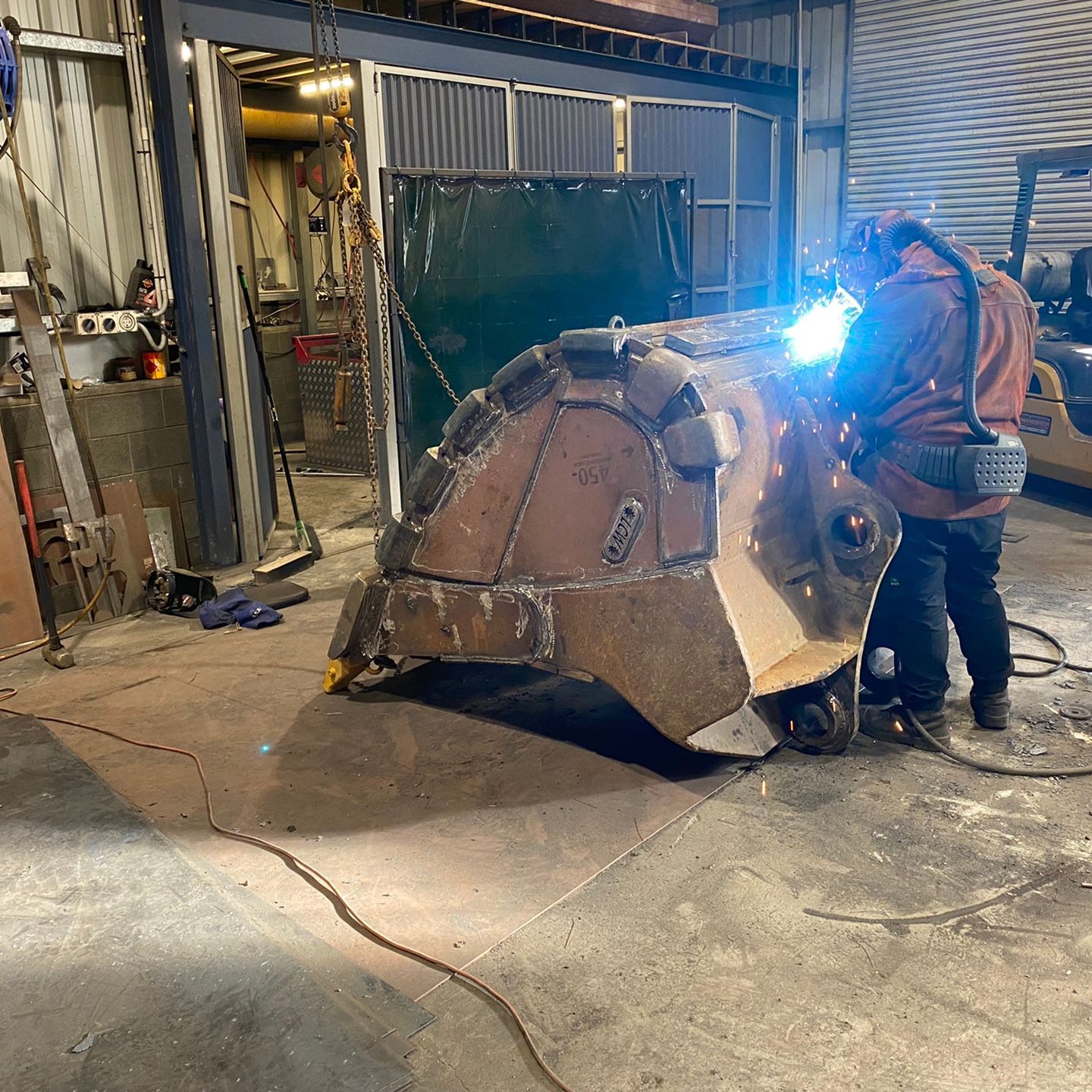 Worker welding a large metal structure inside an industrial workshop, bright blue arc light visible.
