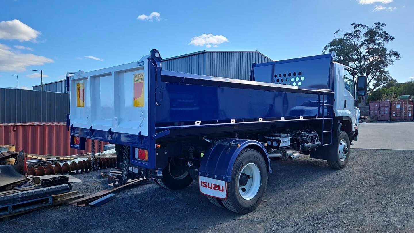 Blue dump truck parked on gravel beside shipping containers under a sunny sky