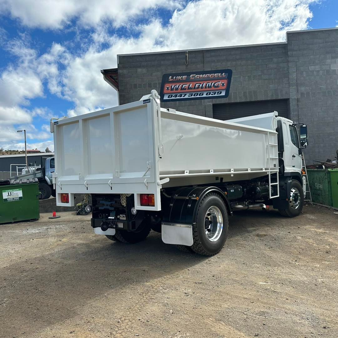 White dump truck parked outside an auto repair shop under a partly cloudy sky