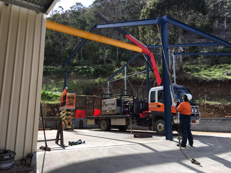 Orange-and-white crane truck lifting steel beams beside a building, with a worker nearby