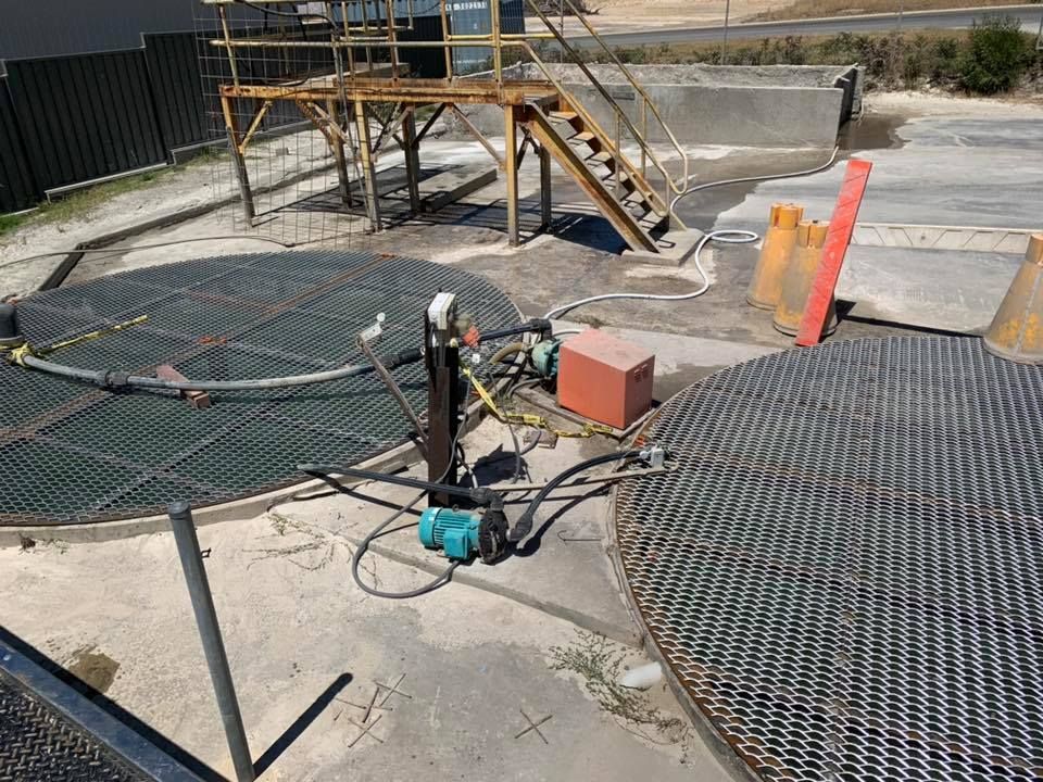 Industrial work site with pumps and hoses on concrete, surrounded by large black mats and a small metal stair platform
