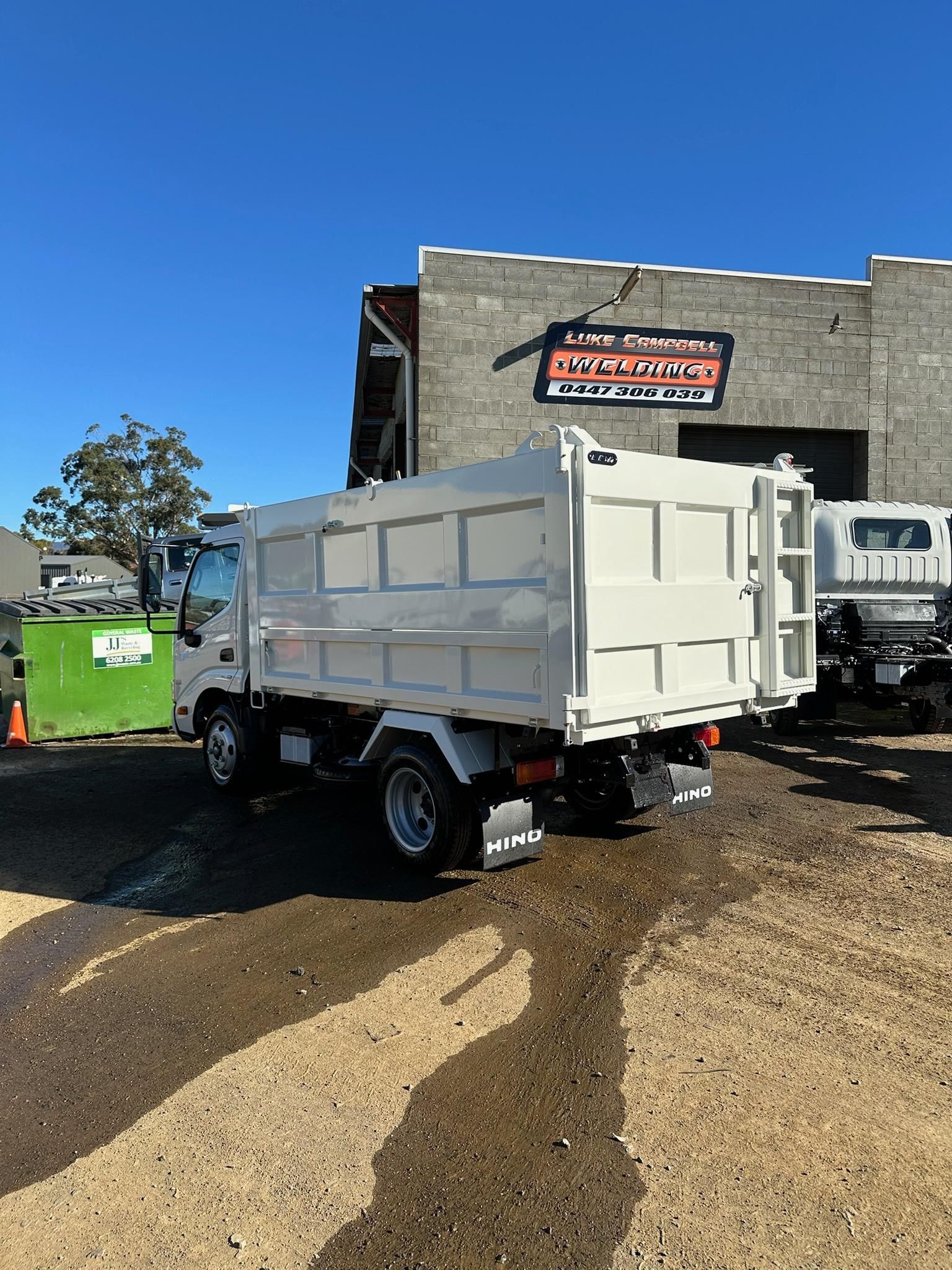 White dump truck parked on muddy ground beside a building under a clear blue sky.