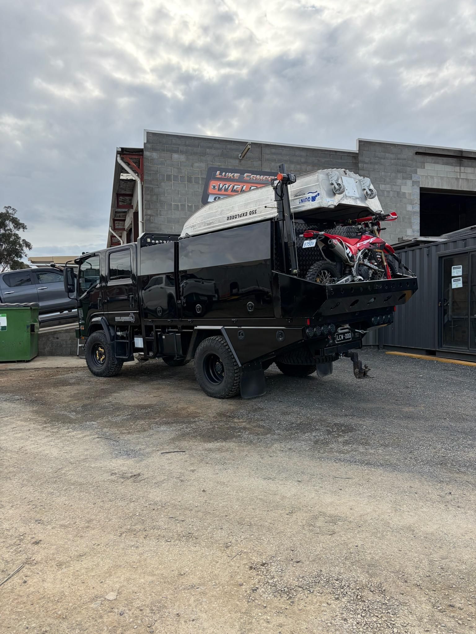 Black utility truck with a cargo bed and red equipment parked on gravel beside a building