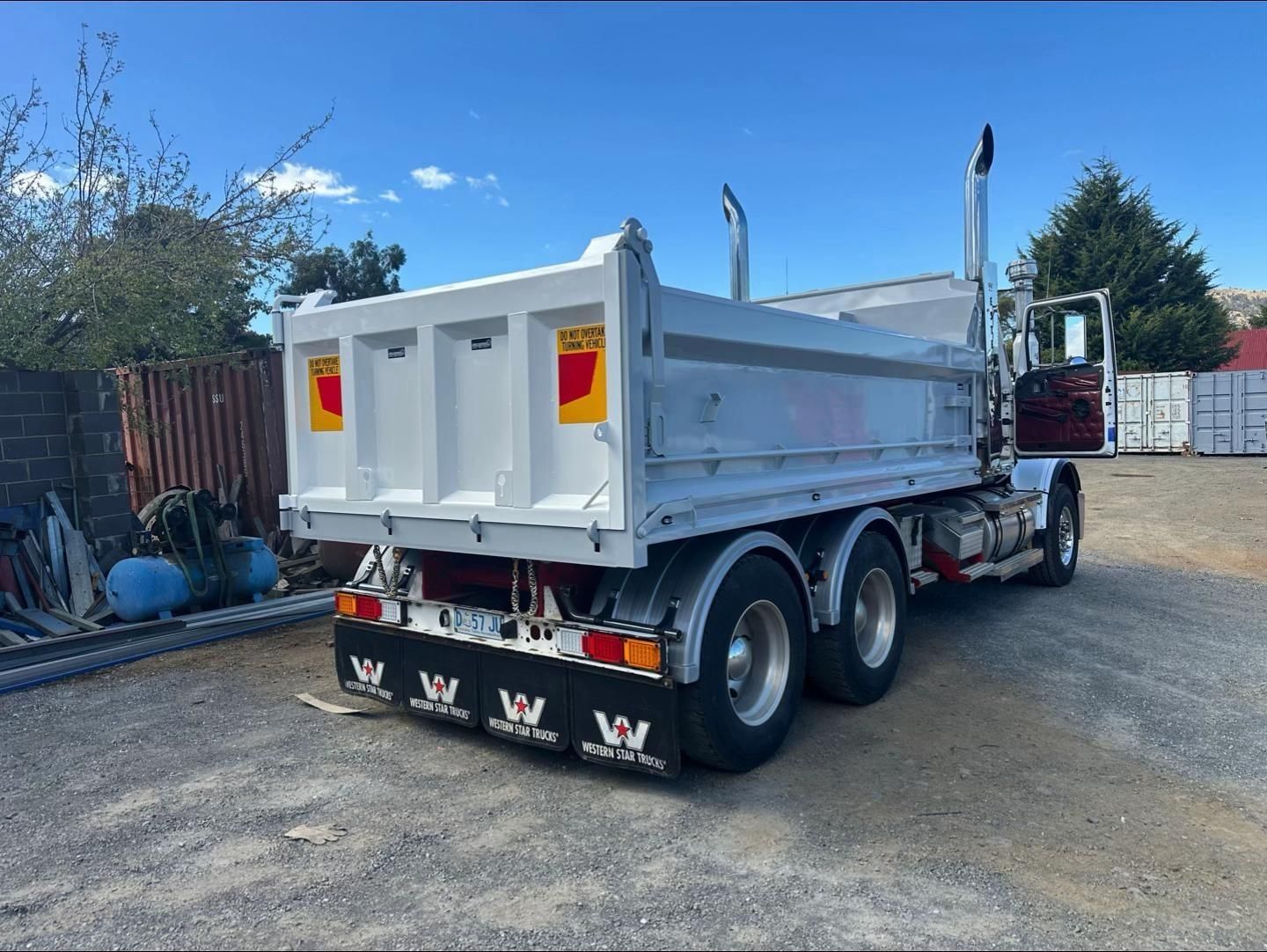 Grey dump truck parked on a gravel lot under a blue sky