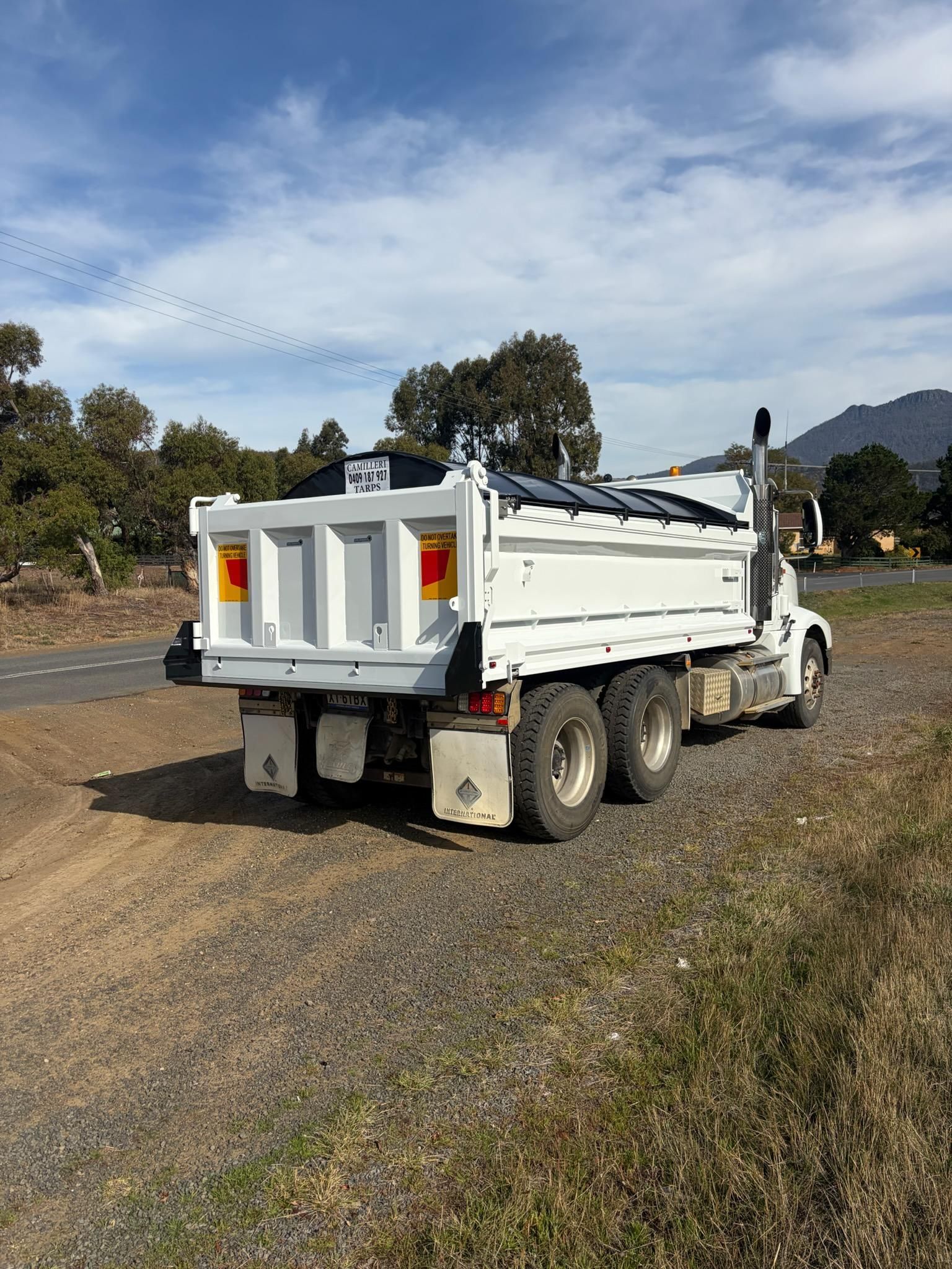 White dump truck on a dirt road in a rural area under a cloudy sky
