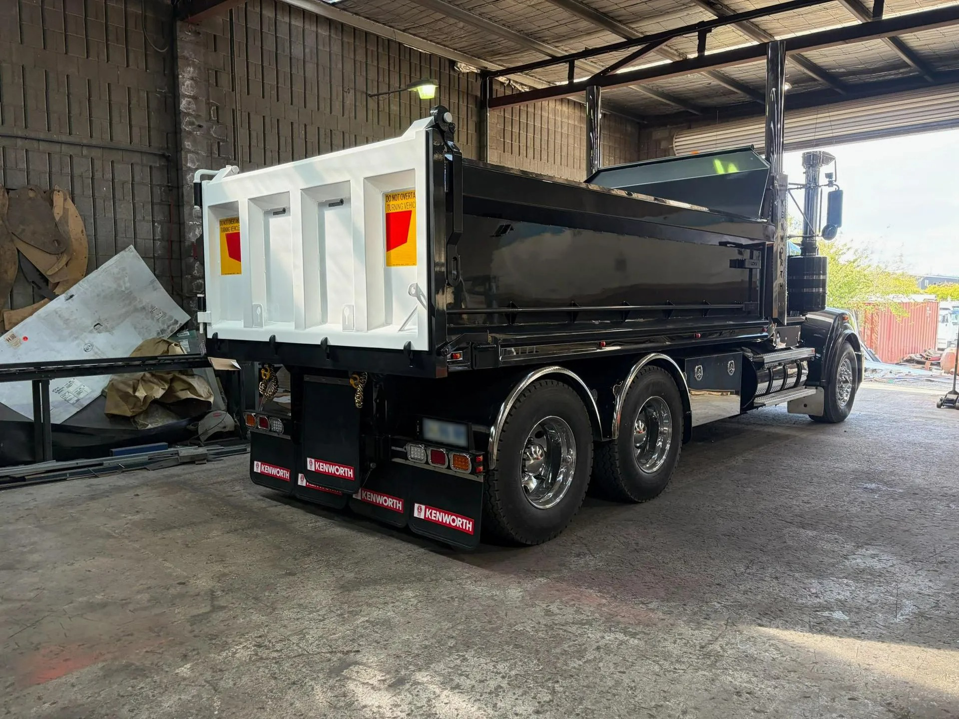 Rear view of a white dump truck in a warehouse, with its bed raised and loaded with dark material.