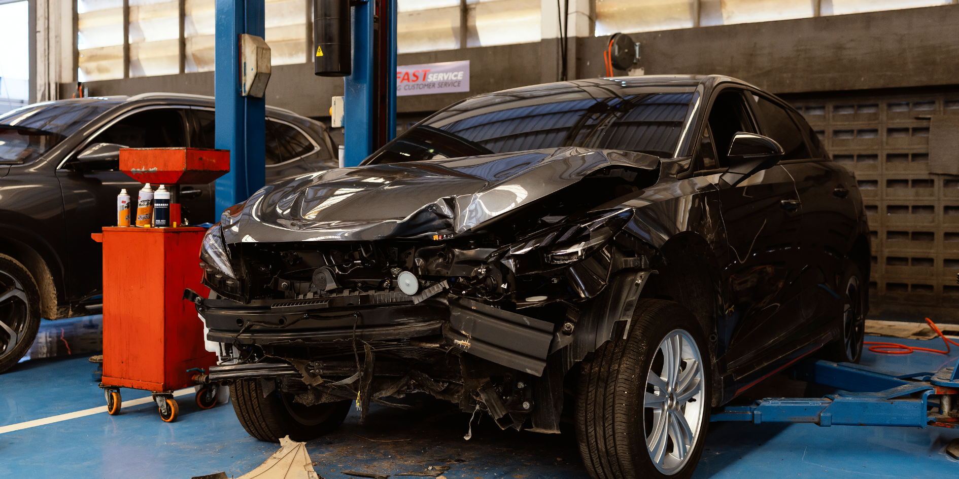Damaged black SUV in an auto repair shop with the front end crushed and hood bent up.