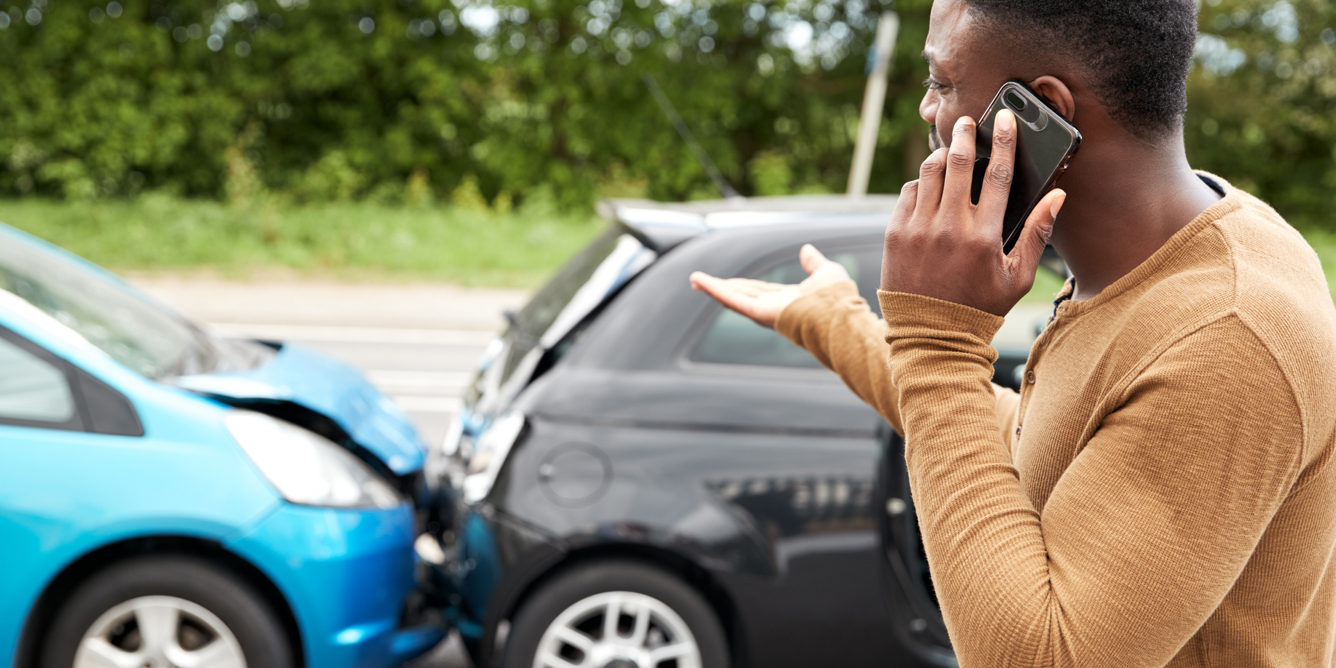 Damaged teal car with a dented front end and a person’s arm reaching from the window