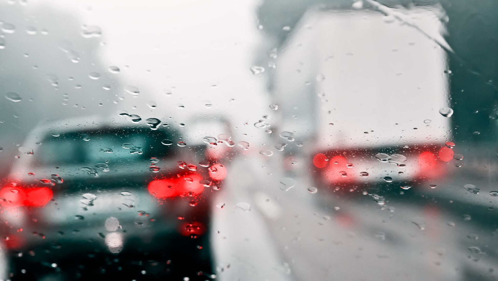Rainy highway scene with car and truck, raindrops on windshield, blurred background.