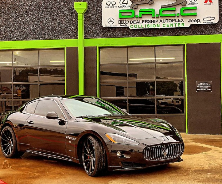 A black Maserati GranTurismo parked in front of a collision center with a green and black sign.