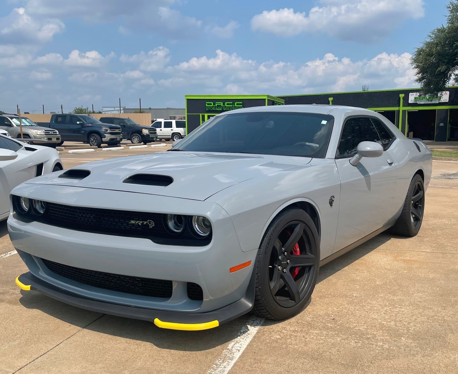A gray Dodge Challenger parked outdoors on a sunny day. It has black wheels, red brake calipers, and a yellow front splitter.