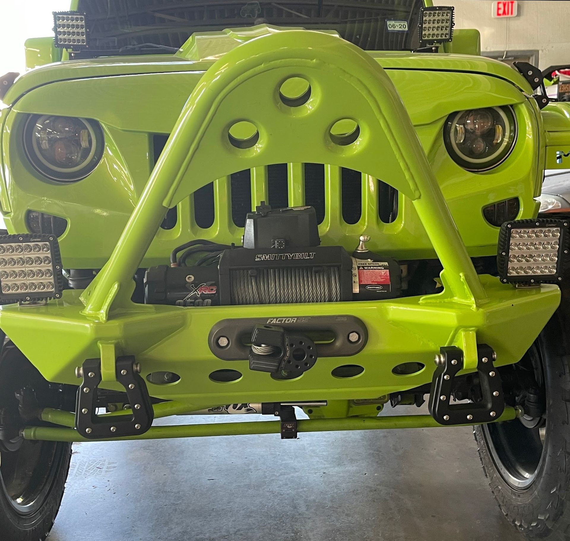 Lime green Jeep with a customized bumper, winch, and LED lights. The Jeep is indoors.