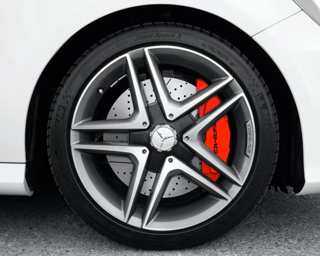 Close-up of a white car wheel with a multi-spoke silver and black rim, a red brake caliper, and a black tire.