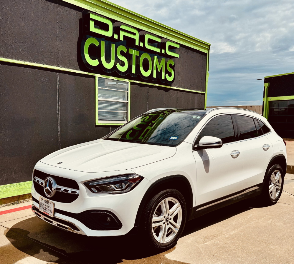 White Mercedes SUV parked in front of D.A.C.C. Customs, a shop with a black exterior and green accents.