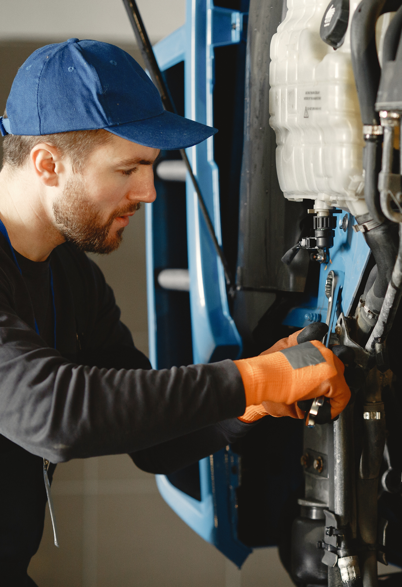 Mechanic using a power drill to repair the front bumper of a gray car in a garage