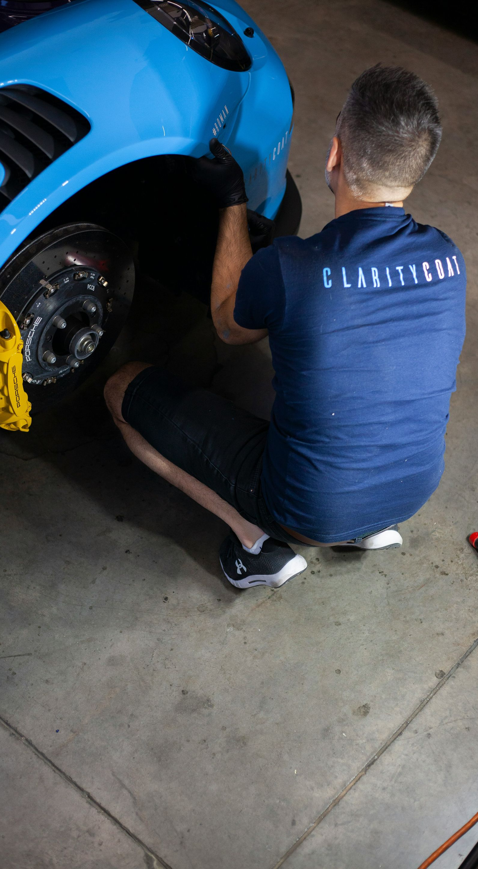 Person kneeling beside a blue sports car, inflating a front tire at night.