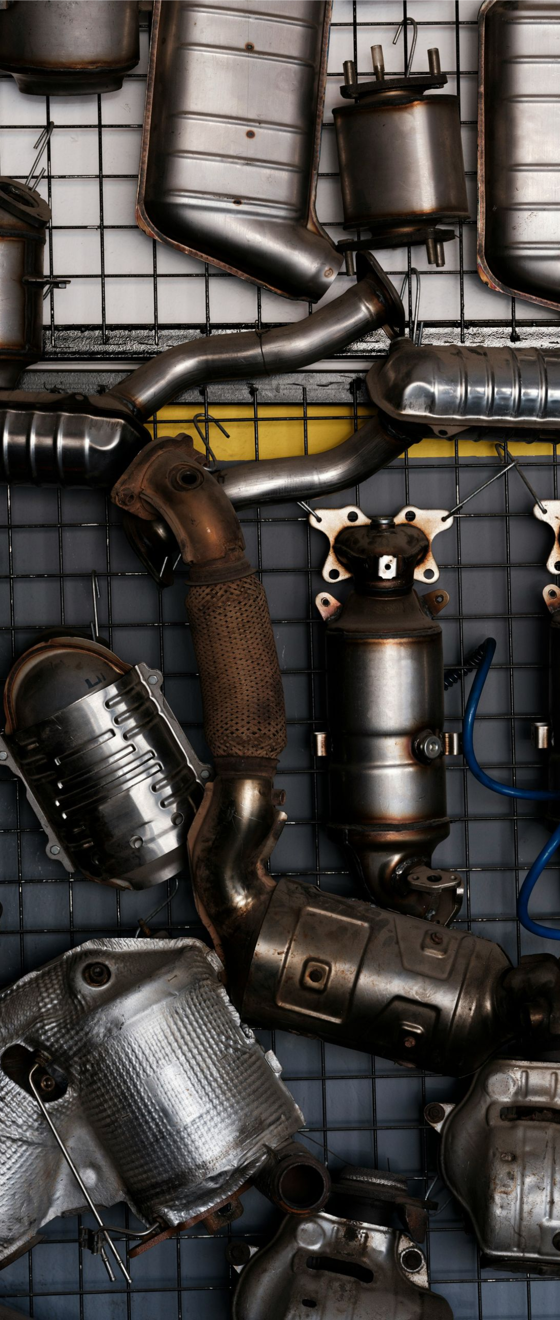 A large collection of metal automotive catalytic converters arranged on a wall-mounted wire grid.
