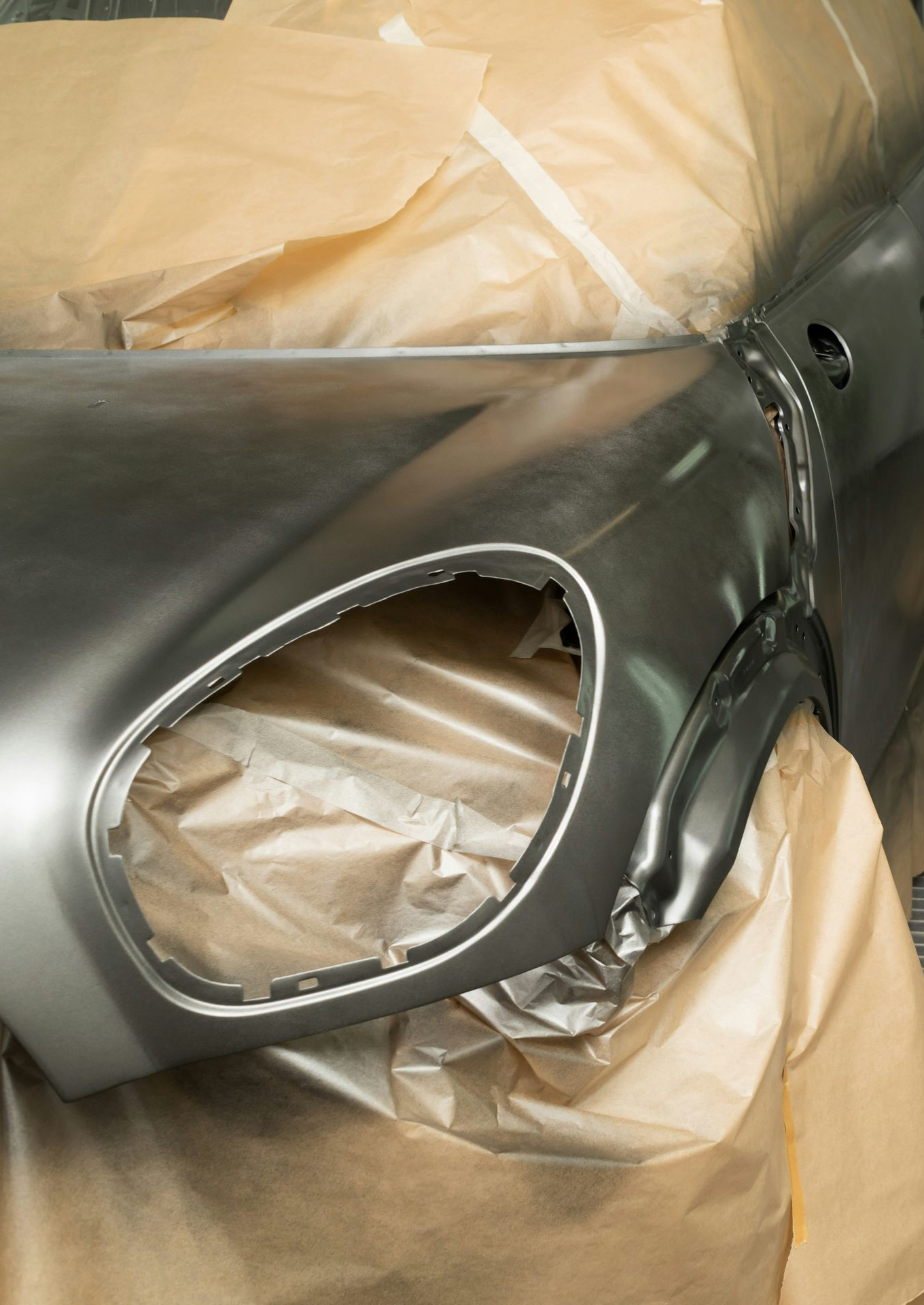 Primered silver car body panel with a circular headlight opening masked for painting