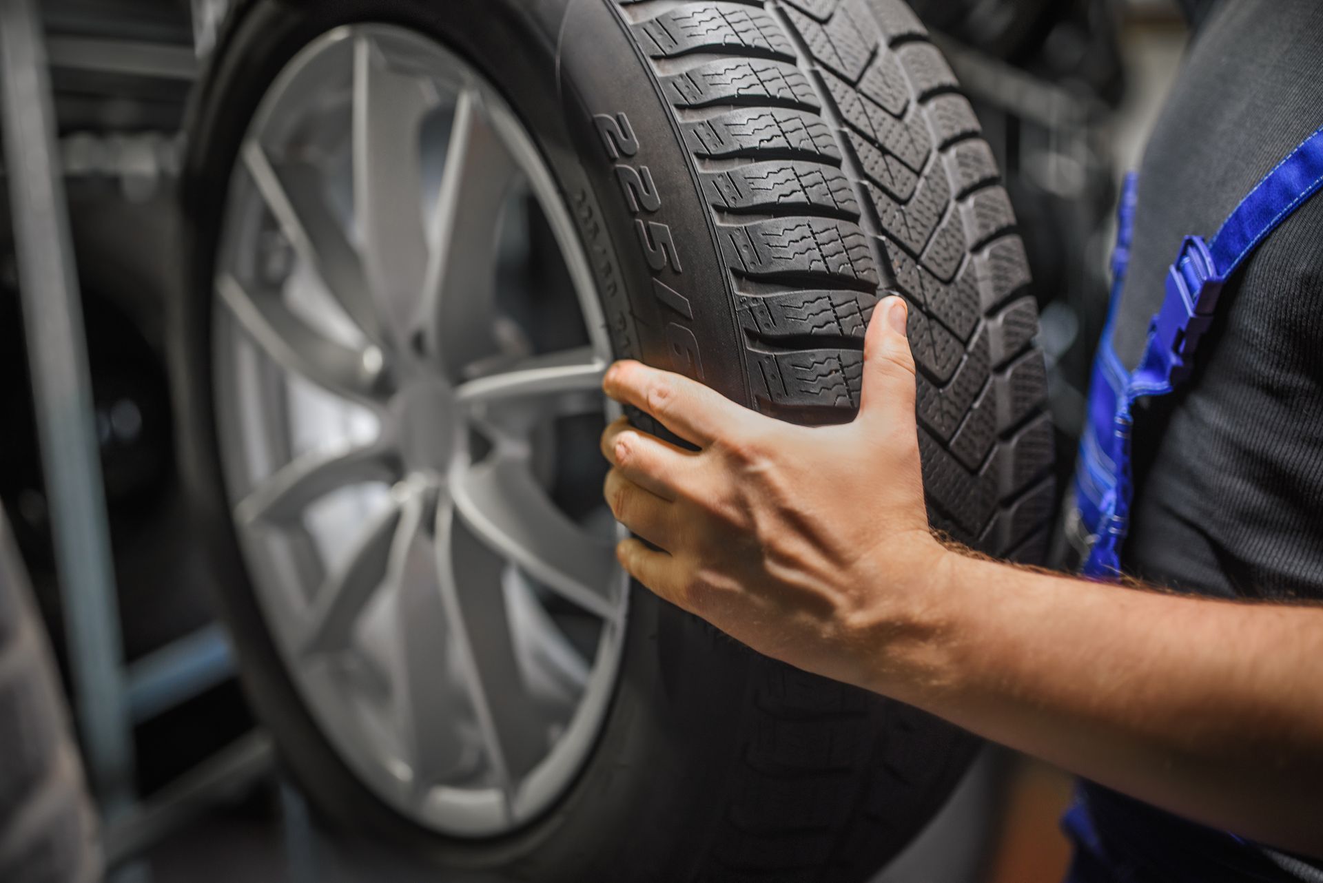 Person holding a car tire, likely in a garage. The tire is mounted on a silver rim.