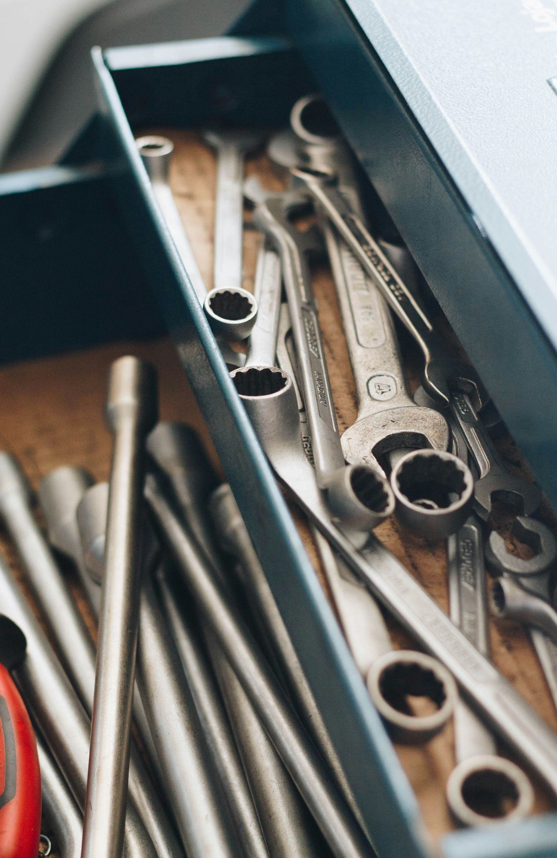 A metal toolbox drawer filled with an assortment of metallic wrenches and socket tools.