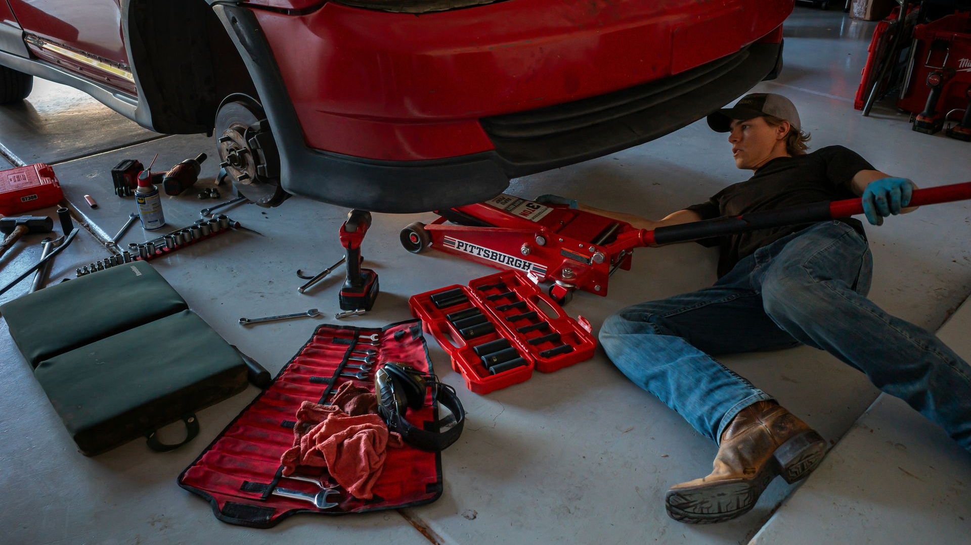 Mechanic lying under a red car, surrounded by tools and removed parts in a garage