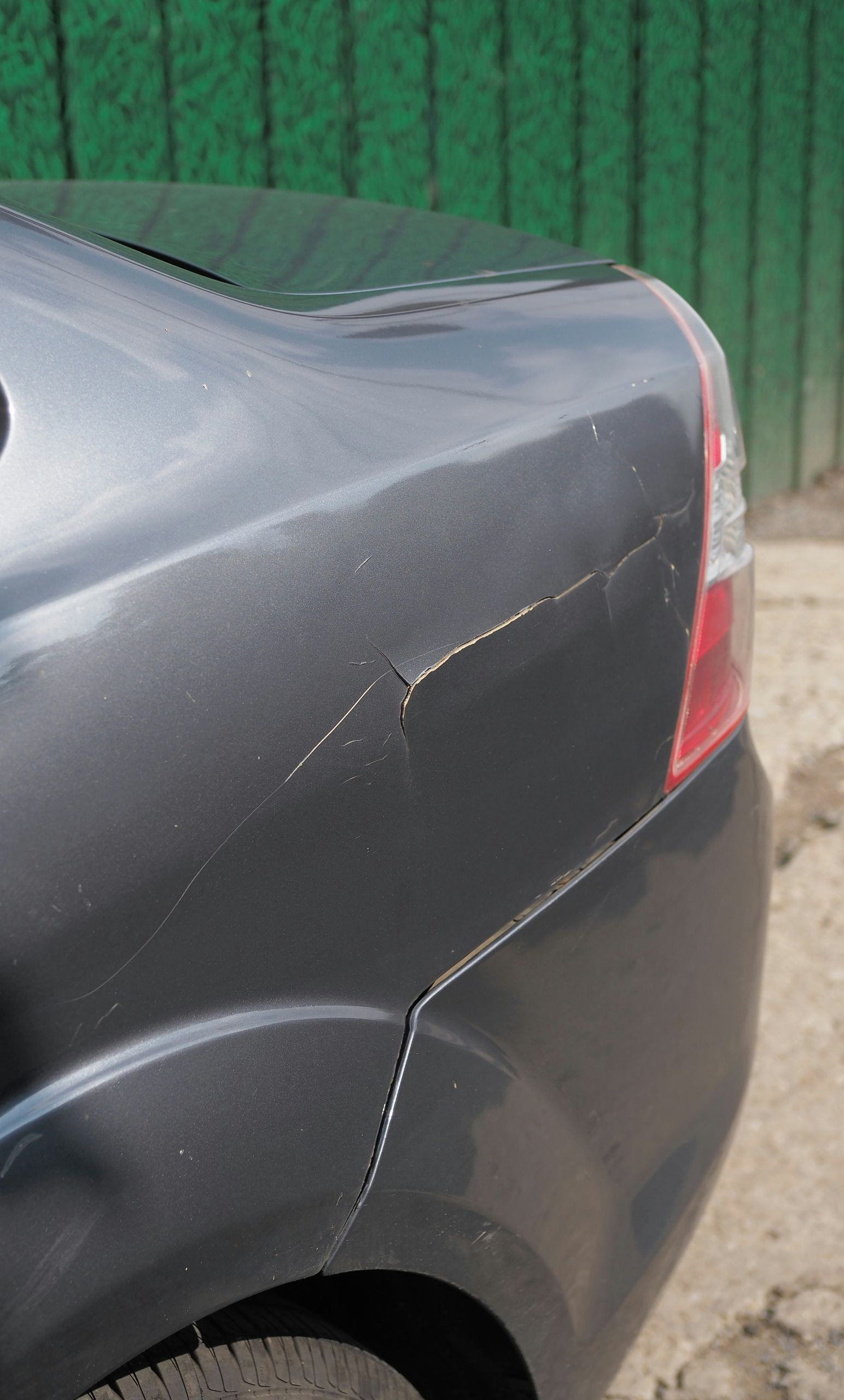 A close-up view of the rear quarter panel of a gray car showing deep scratches and paint damage near the tail light.
