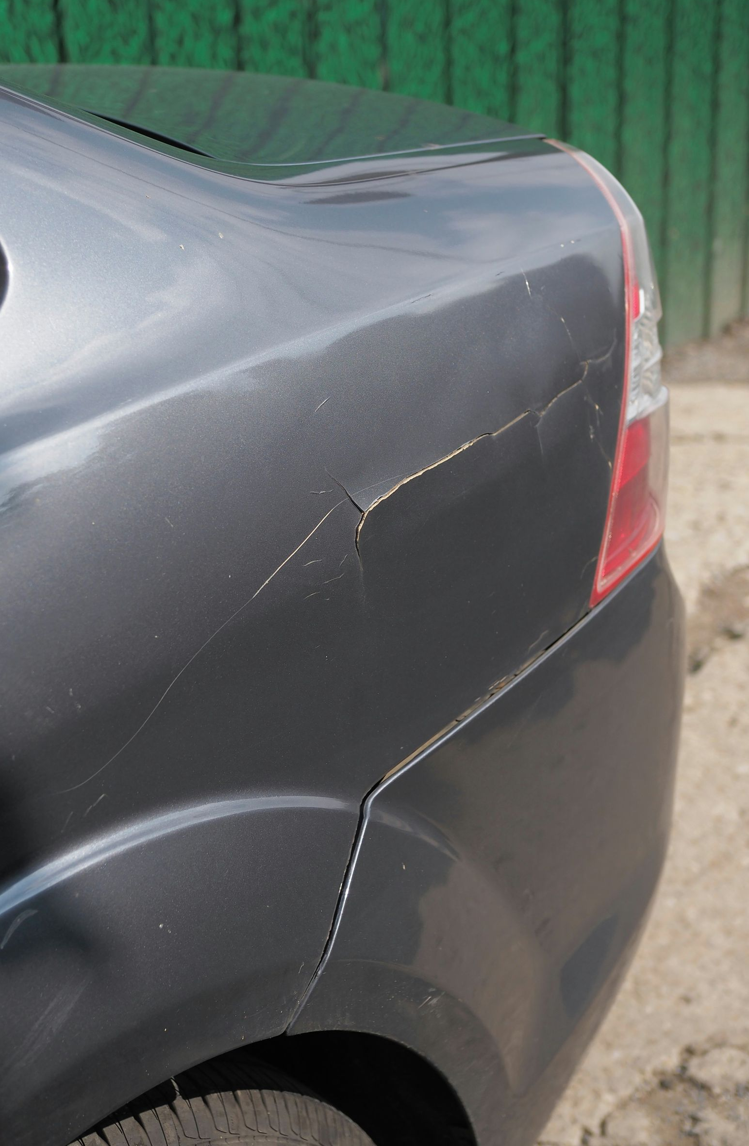 A close-up view of the rear quarter panel of a gray car showing deep scratches and paint damage near the tail light.