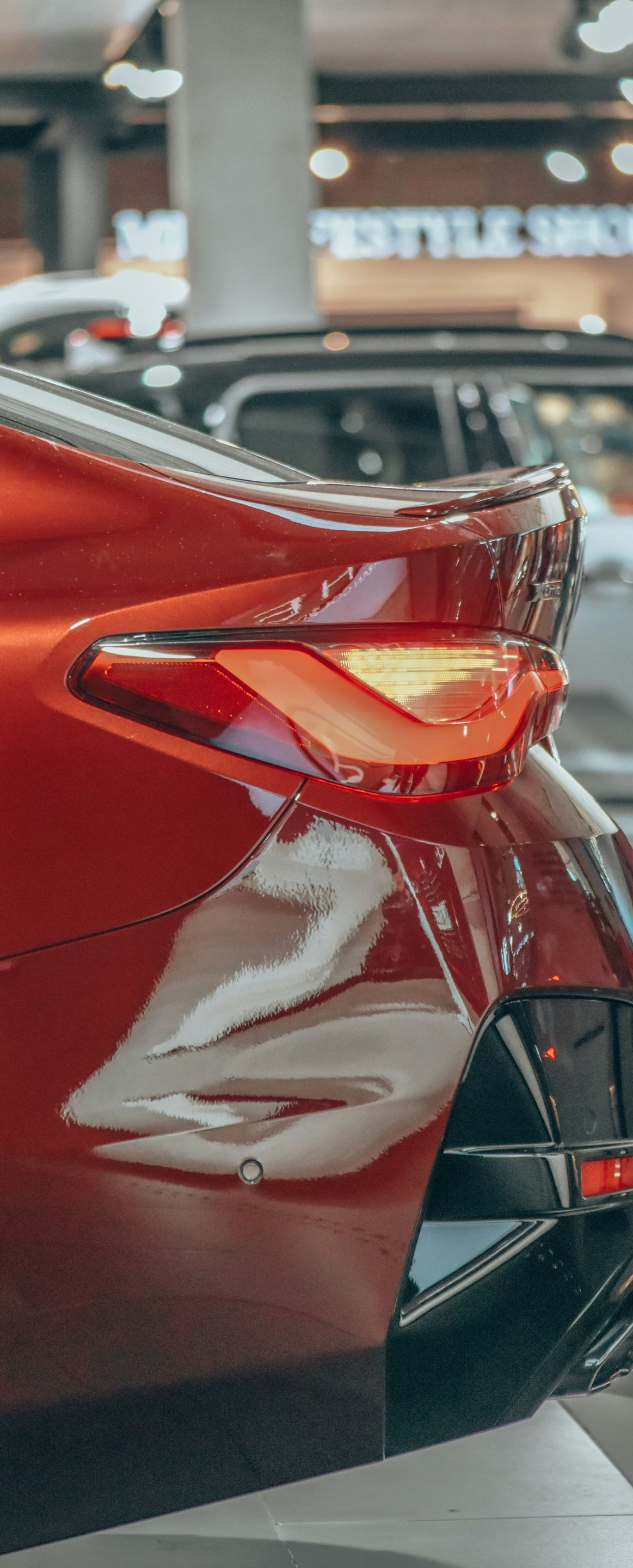 Rear view of a red sports car in a showroom, highlighting its taillight and sleek body.