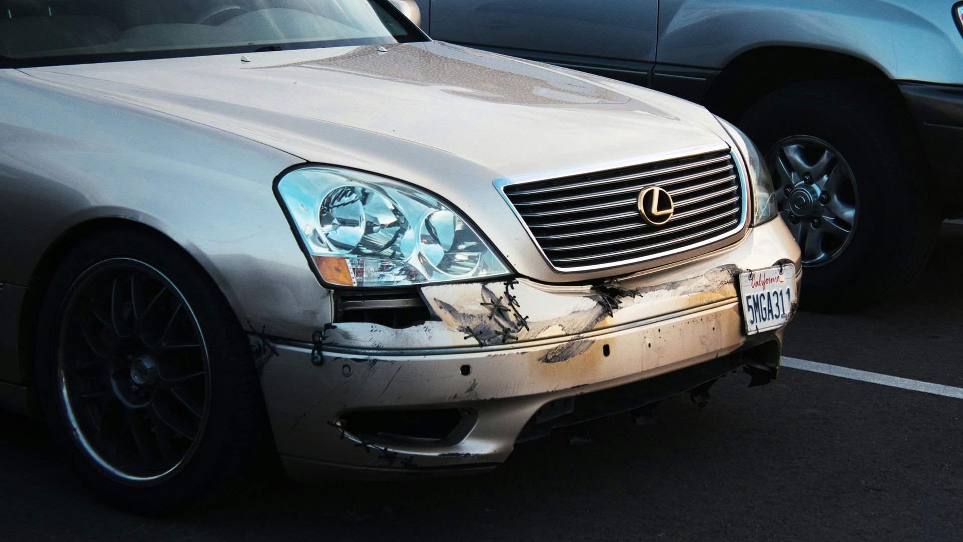 White Lexus sedan with a damaged front bumper and headlight in a parking lot