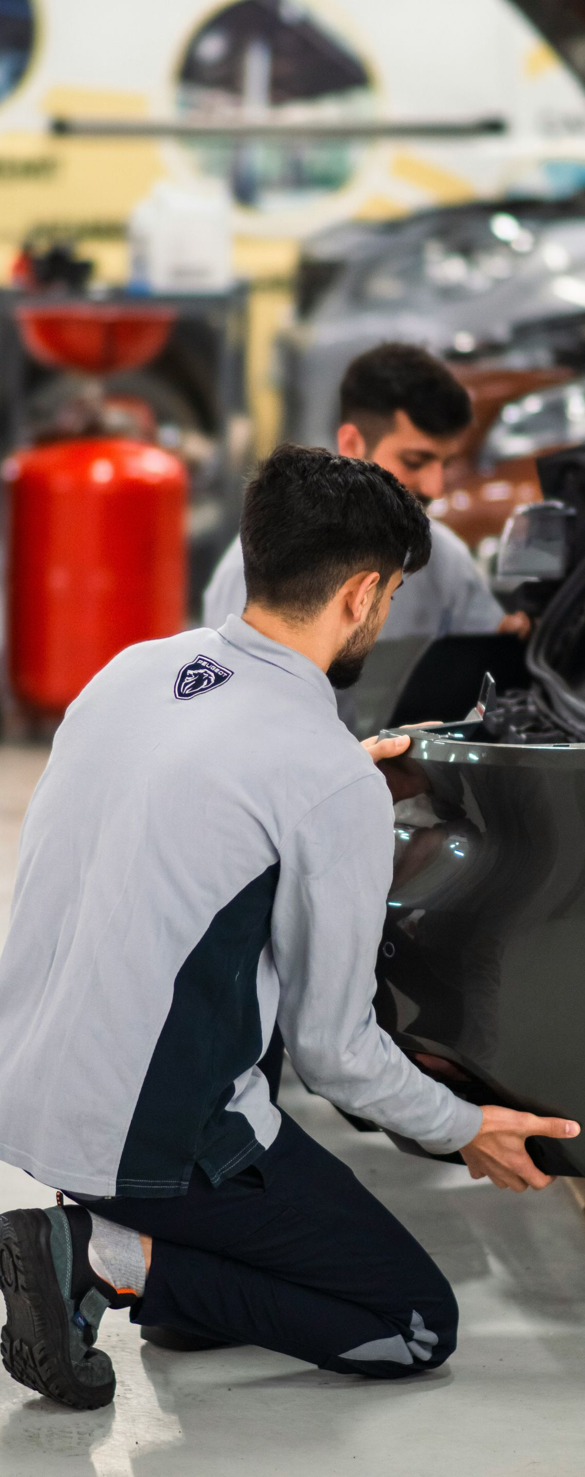 Mechanic kneeling beside a black car in a garage, inspecting the lower side panel.