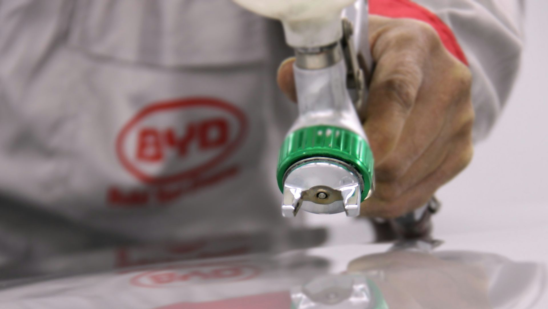 Person using a spray gun to paint a glossy white car surface