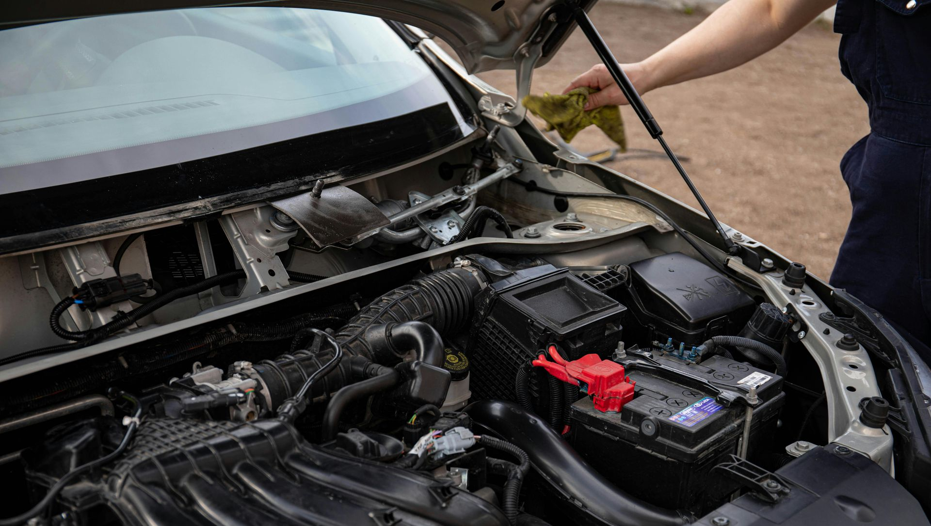 Open car engine bay with a person pointing at the battery
