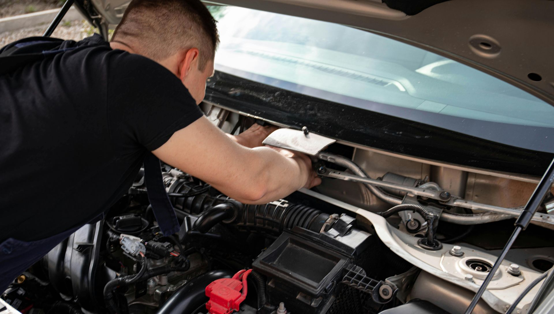 Mechanic working under a car’s hood, inspecting the engine bay with tools.