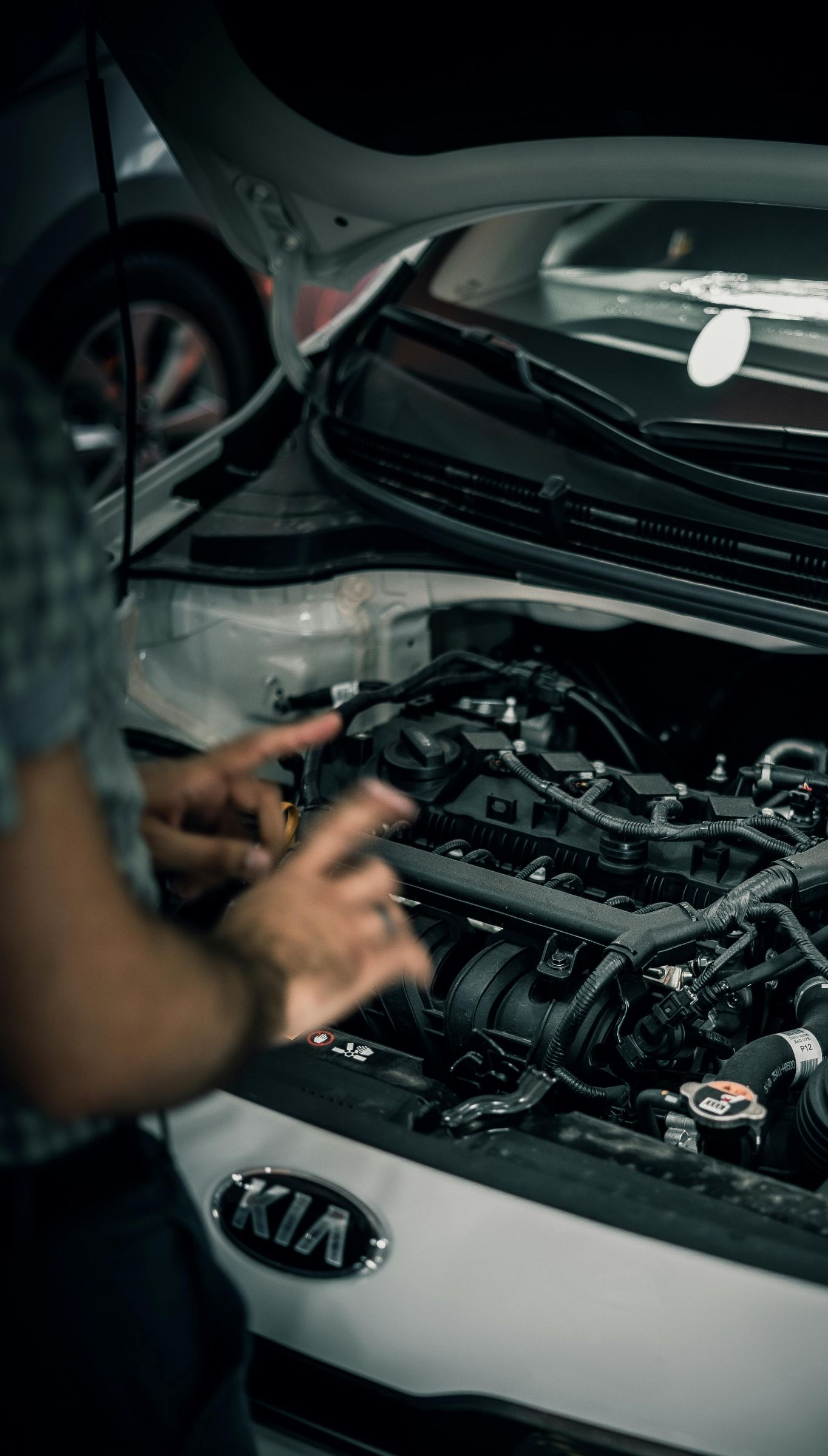 Person working on a Kia car engine with the hood open at night
